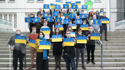 Gruppenfoto vom Landesdelegiertenrat, die Teilnehmer*innen halten Schilder hoch, auf denen sie ihre Solidarität mit der Ukraine ausdrücken.